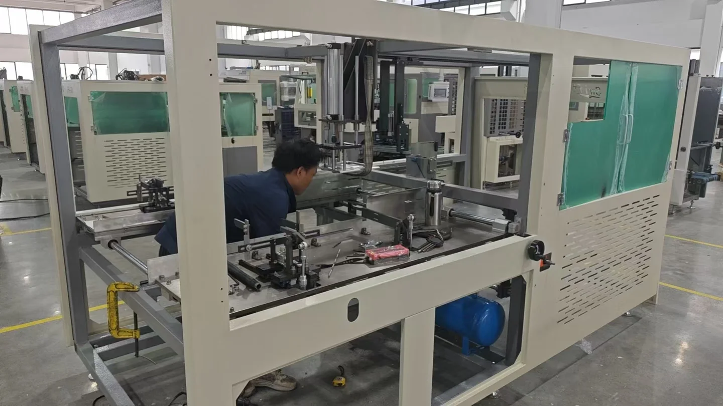 A worker beside a partially assembled box forming machine inside the production workshop