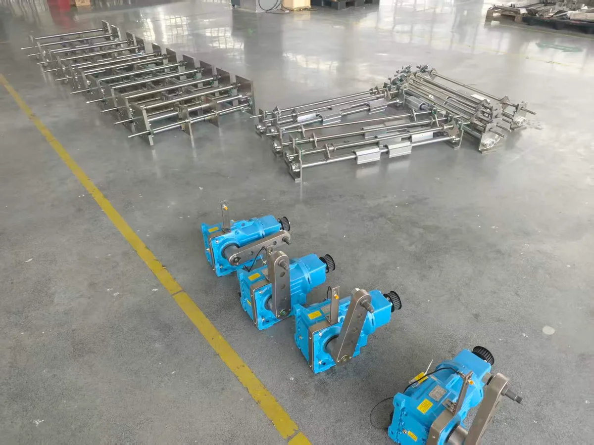 Gruppi di rulli in acciaio inossidabile e motoriduttori blu parcheggiati in fila all'interno di una segnaletica gialla sul pavimento