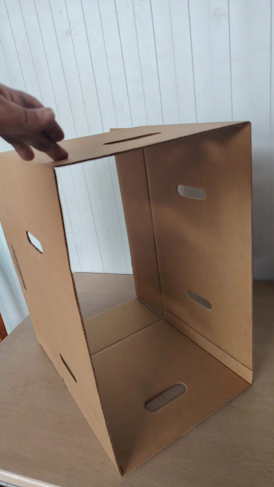 Actual apple carton held on its side to show folded panel overlaps and elongated ventilation slots