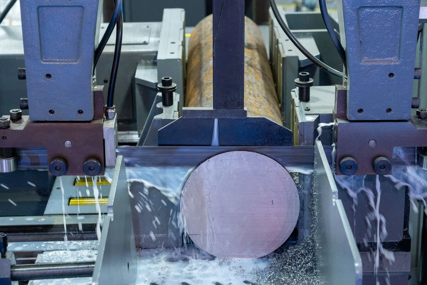 Industrial band saw cutting a solid round metal bar held between machine guides, with coolant at the cut