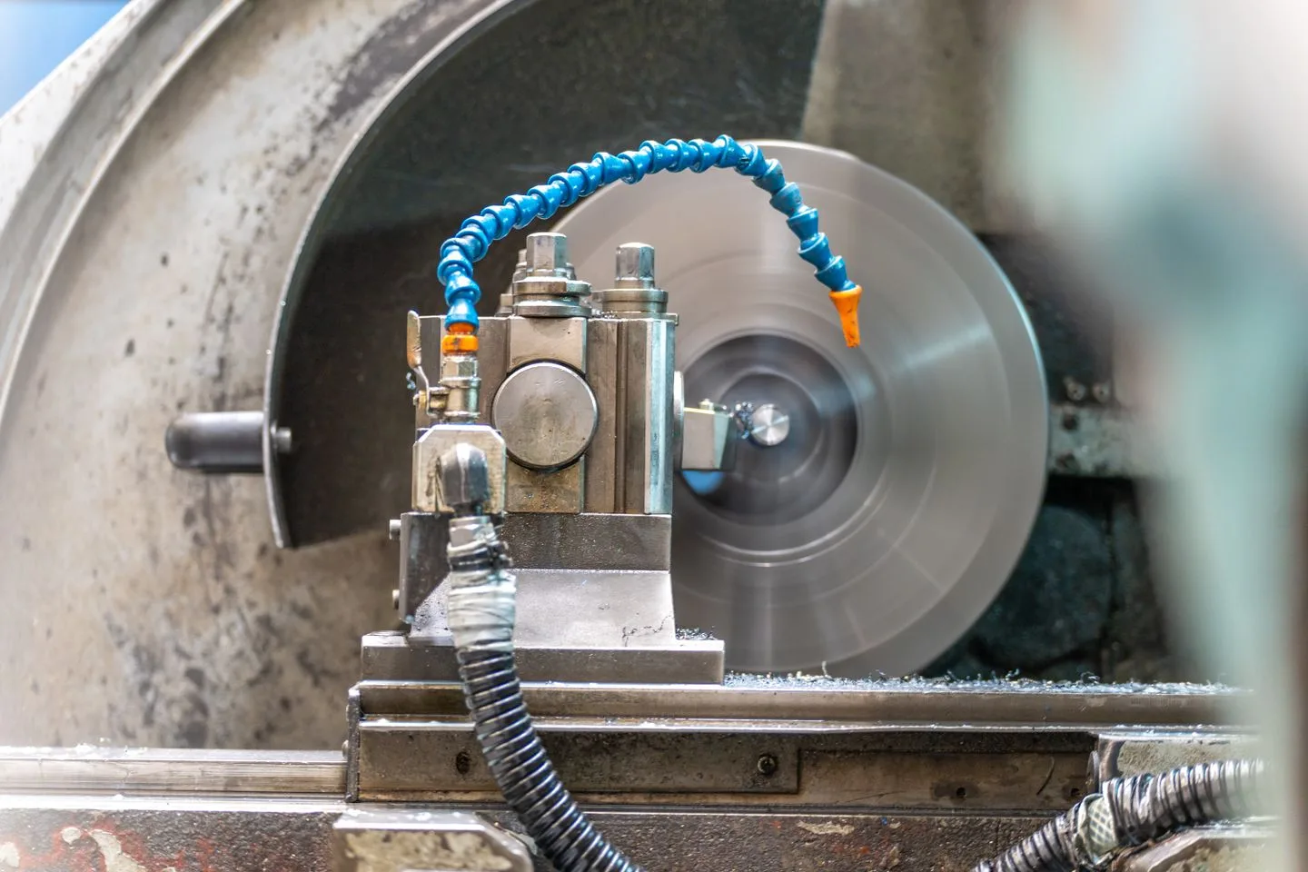 Lathe tool positioned at a rotating cylindrical metal workpiece, with a coolant nozzle above the cutting area