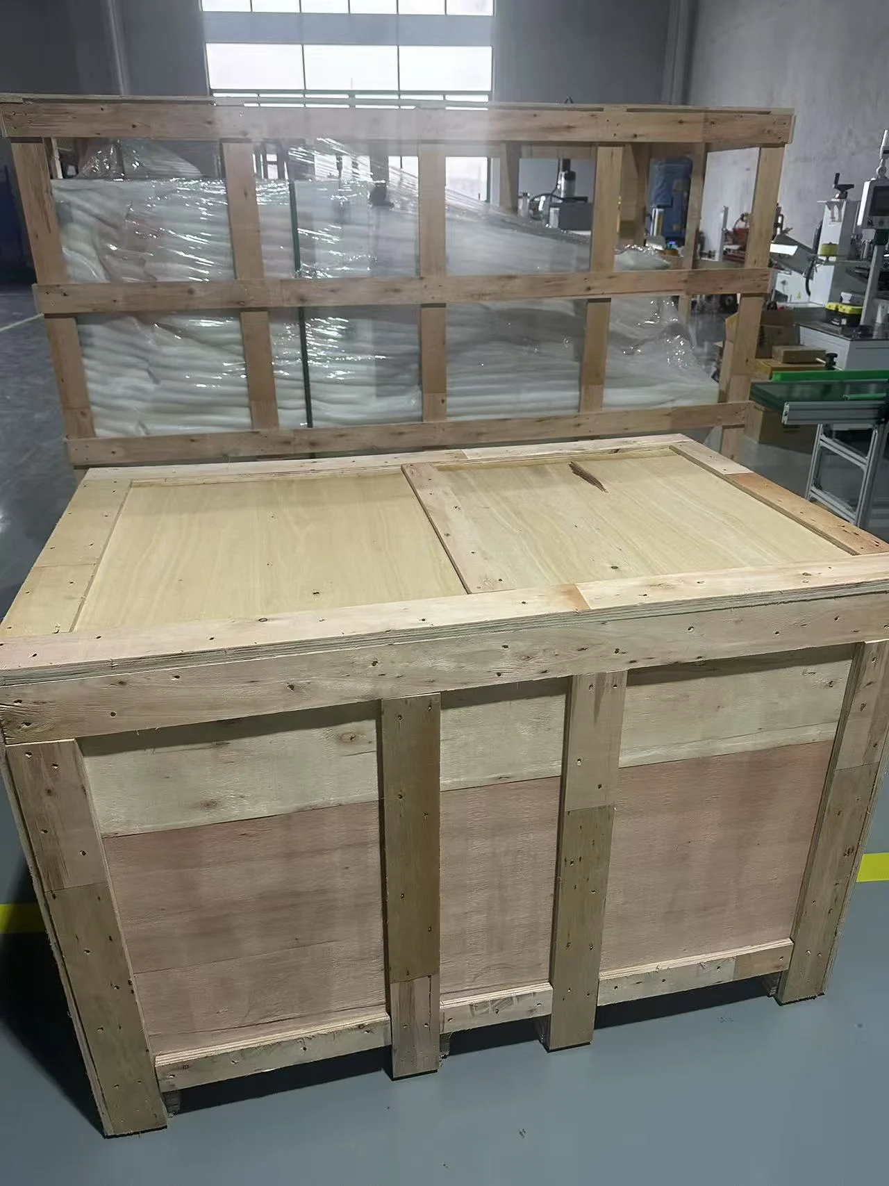 Closed wooden shipping case in front of a timber frame containing protective wrapping in the packing area