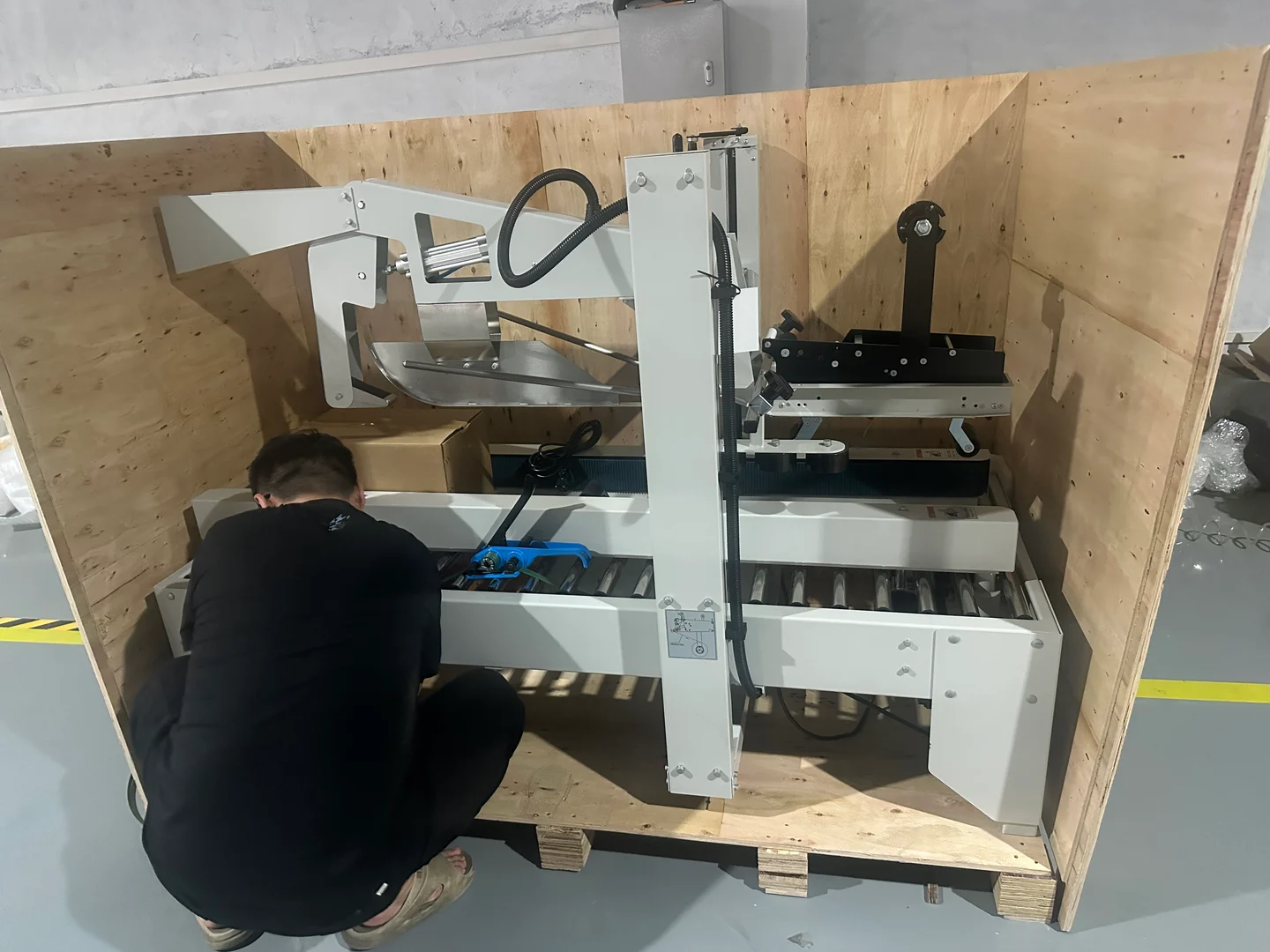 Worker preparing a 5050 machine inside an open wooden shipping case, with the machine frame and roller bed visible